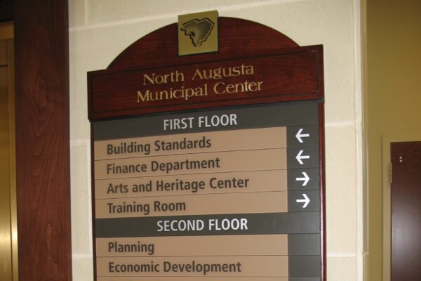 A directional sign inside the North Augusta Municipal Center listing various departments on different floors: Building Standards, Finance Department, Arts and Heritage Center, and Training Room on the first floor; Planning, Economic Development, Engineering, and Stormwater Management on the second floor; and Mayor, City Administrator, City Attorney, City Clerk, Council Chambers, Council Conference Room, Historical Resources, and Gallery on the third floor.