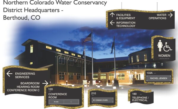A nighttime image of the Northern Colorado Water Conservancy District Headquarters in Berthoud, CO. The building is lit with warm lights. Various black and gold signs point to different departments and rooms, including conference rooms, IT, water operations, and restrooms.