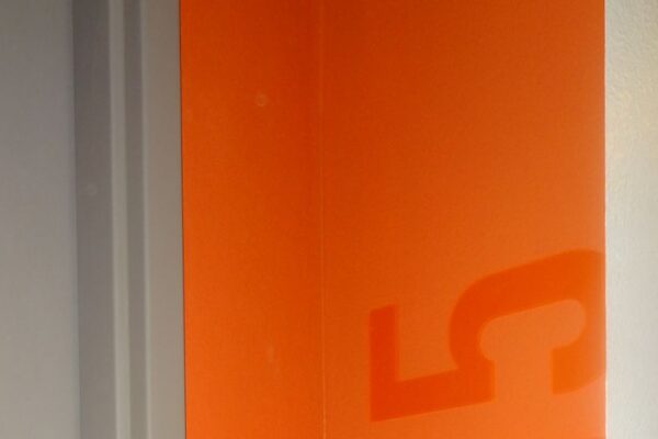 A door with a silver handle and lock is partially open, revealing an orange wall inside with the number "715" written vertically in large, glossy numbers. The door frame is grey.
