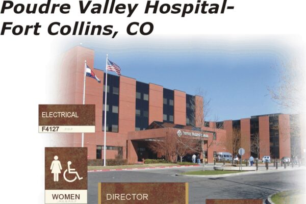 Image of Poudre Valley Hospital in Fort Collins, CO. The hospital is a large red-brick building with American and Colorado flags. There are various signs in the foreground showing locations within the hospital: Electrical, Women's restroom, Director's office, and F4671.