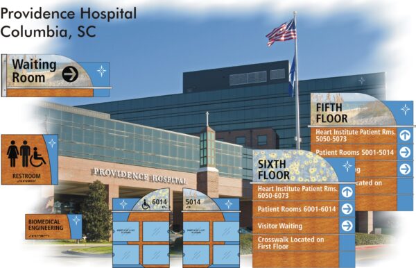 An image showing Providence Hospital in Columbia, SC, with multiple signs indicating directions to various facilities such as the waiting room, restroom, biomedical engineering, and specific patient rooms on the fifth and sixth floors. An American flag waves in front.
