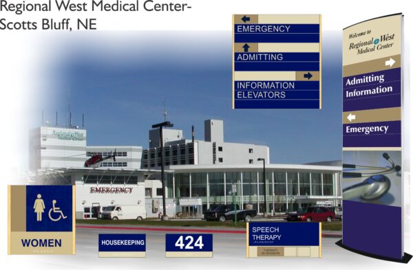 Image of Regional West Medical Center in Scotts Bluff, NE. The hospital building has multiple entrances, with prominent signs for Emergency, Admitting, and Elevators. Additional signs include Women's health, Housekeeping, Room 424, Speech Therapy, and a directional stand.