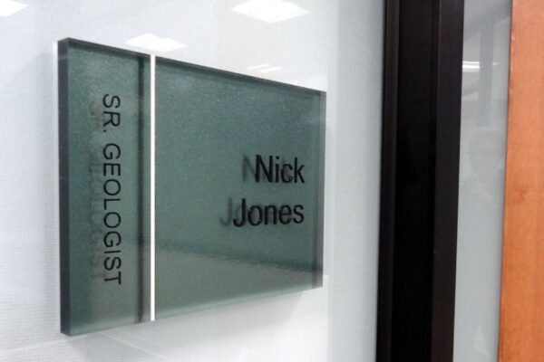 Office nameplate reading "SR. GEOLOGIST" and "Nick Jones" on a frosted glass panel beside a door.