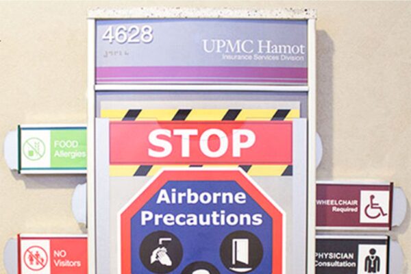 A sign on a hospital wall with various tags: Room number 4628, UPMC Hamot, "STOP Airborne Precautions" with icons indicating a mask, no visitors, wheelchair required, physician consultation, medical equipment required, and food allergies.