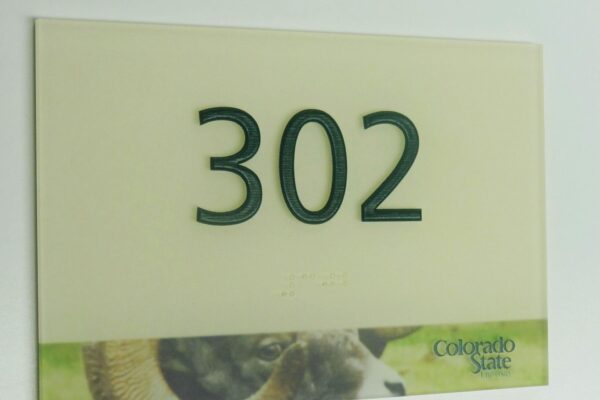 A room number sign displays the number "302" in raised green font. The lower part of the sign features a partial image of a ram and includes the "Colorado State" logo.