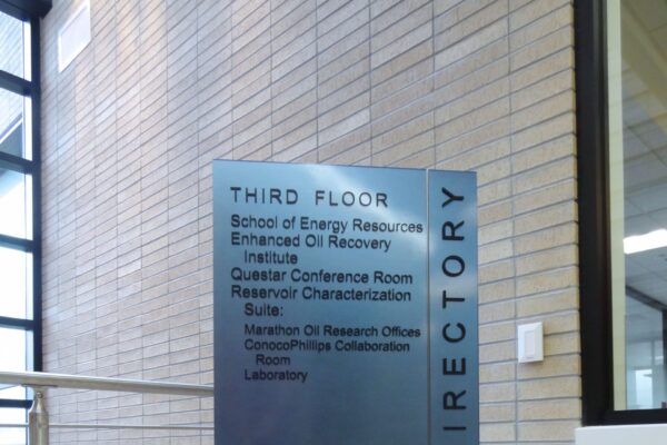 A metallic directory sign on a stand listing the locations of various rooms on the third floor, including the School of Energy Resources, Enhanced Oil Recovery Institute, Center for Energy Economics and Public Policy, Center for Fundamentals of Subsurface Flow, and others.