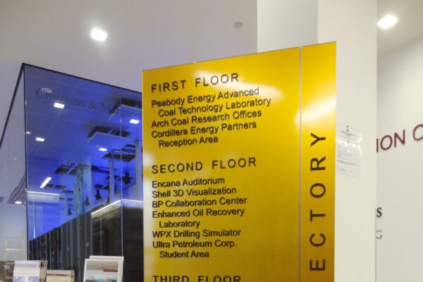 A yellow directory sign in a building lists the floor details: First Floor - various energy and environmental labs, and offices; Second Floor - aviation, space labs, and resources; Third Floor - systems, transportation resources, and cybersecurity.