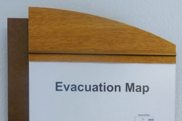 A wall-mounted evacuation map framed in wood shows a detailed layout of a building with various rooms numbered. The areas are color-coded, and exits are marked. The map has a title "Evacuation Map" at the top.