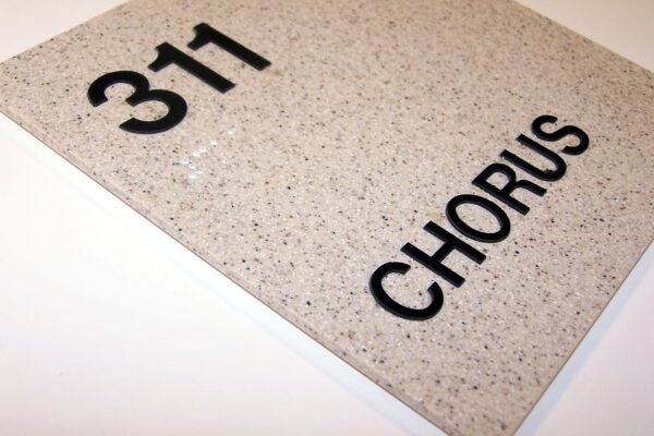 A marble-like sign showing room number 311 with the word "CHORUS" written in large black letters below it. The sign is placed at an angle on a white surface.