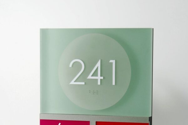 A room sign displaying "241" at the top, followed by panels indicating "FALL RISK" (red with a falling figure icon), "VISITORS: Please Check-In at Nurse Station" (red with two visitor icons), "NOTHING BY MOUTH" (purple), "CONTACT ISOLATION" (blue), and "VISION IMPAIRED" (yellow).