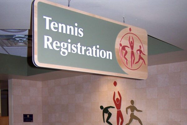 A tennis registration area at a sports center. The desk has a decorative fall-themed garland and a sign above reads "Tennis Registration." The wall behind the desk features the sports center's logo with vibrant figures and the name "Visionsport Sport Center.