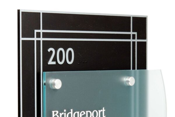 A black and silver sign displays the text "200" at the top and "Bridgeport Dental" in white letters on a frosted glass panel affixed to the sign. The design includes a series of thin horizontal and vertical lines for a modern look.   Etched Zinc backplate, changeable green-glass acrylic nameplate. 