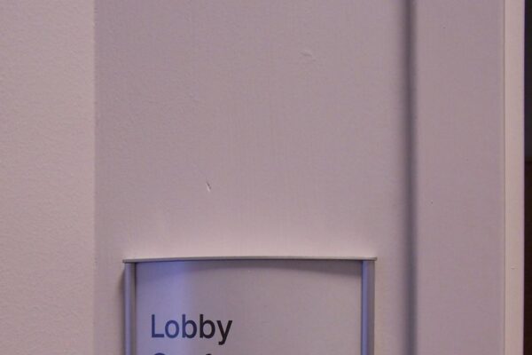 A small rectangular wall sign reads "Lobby Conference Room" with the number "106" displayed beneath it. The sign is mounted on a light-colored wall, indicating the room's location and purpose within a building.