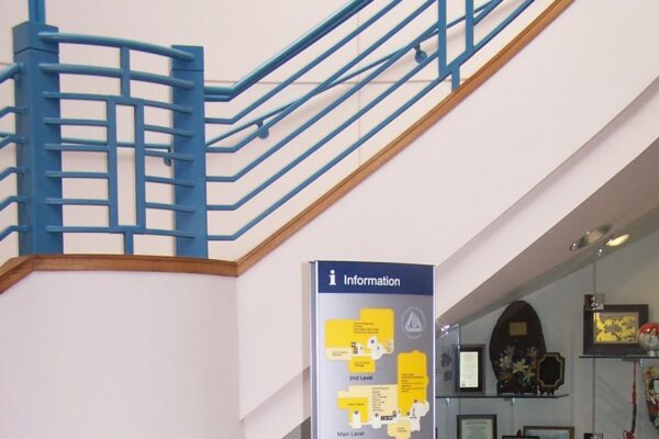 A stand-alone information board with yellow and white details is positioned in the center of an indoor area with tiled flooring and a compass design.