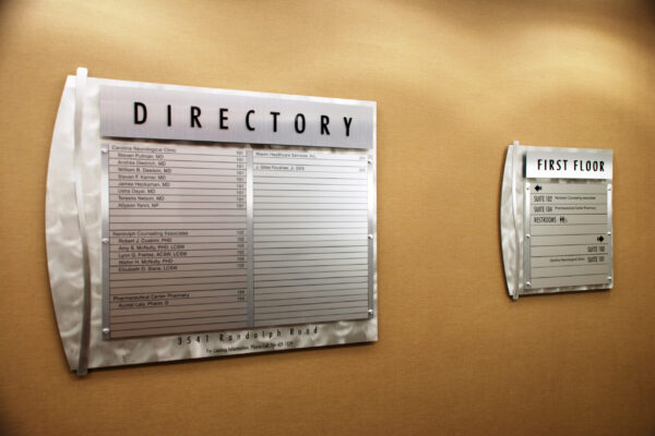 A directory board on the left lists the locations of various departments or offices, while a first floor directory on the right provides a smaller, focused list of locations specifically for the first floor. Both directories are mounted on a beige wall.