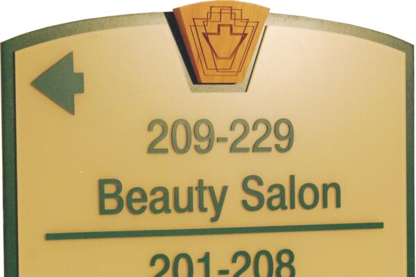 A directional sign with a yellow background and green edges. The sign indicates room numbers and locations: "209-229 Beauty Salon" with an arrow pointing left, and "201-208 Library/Computer Pool/Fitness" with an arrow pointing right.