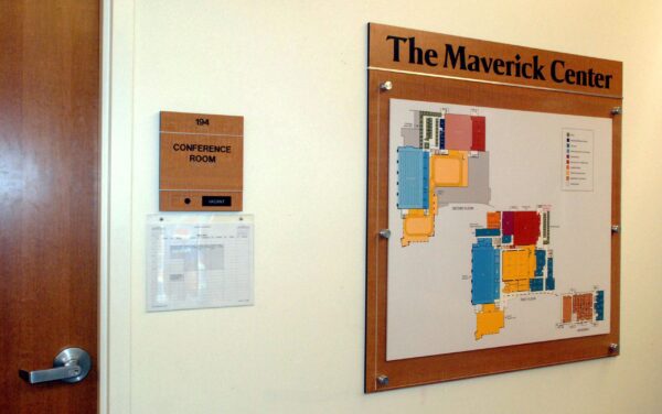 A wall-mounted map of The Maverick Center with various colored sections. To the left, there is a door with a sign that reads "Conference Room" and a small clipped sheet beneath it. A door handle is visible at the bottom left.
