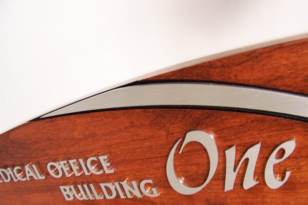 Close-up image of a wooden sign with metallic lettering that partially reads "Medical Office Building One." The focus is on the top edge of the sign, highlighting its curved design and polished wood finish.