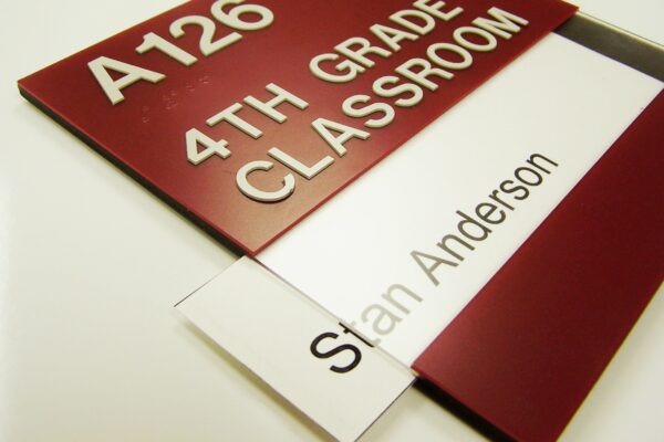A maroon and white classroom sign reads "A126 4th Grade Classroom" at the top. Below it is a nameplate that partially slides out, revealing the name "Stan Anderson.