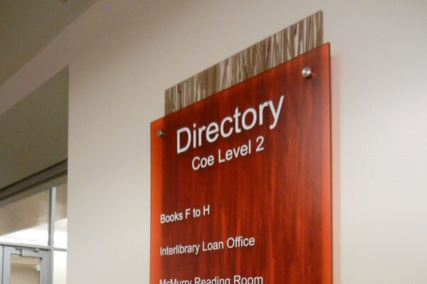 A red wall-mounted directory sign on Coe Level 2 lists several locations: Books F to H, Interlibrary Loan Office, McMurtry Reading Room, Popular Reading Collection, Reference Collection, and Study Rooms 263, 264, & 266. An exit sign is visible below it.