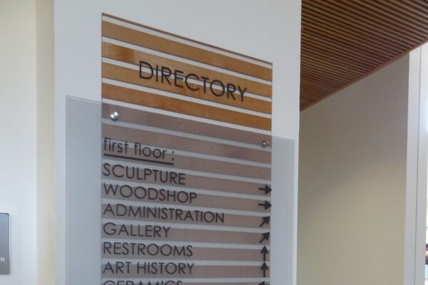 A directory sign in a building lists various locations: Sculpture, Woodshop, Administration, Gallery, Restrooms, Art History, and Ceramics on the first floor; Printmaking, Photography, Graphic Design, Metalsmithing, Foundations A&B, Drawing A&B, and Painting on the second floor.