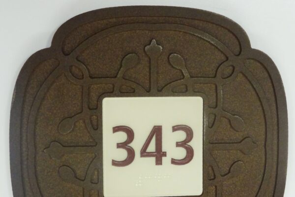 A decorative plaque with an ornate brown border features the number "343" in bold red digits at the center on a white background. The border design includes symmetrical patterns that resemble floral motifs.