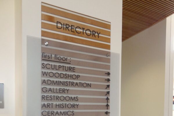 A wall-mounted directory sign lists sections for two floors. The first floor includes Sculpture, Woodshop, Administration, Gallery, Restrooms, Art History, and Ceramics. The second floor lists Printmaking, Photography, Graphic Design, Metalsmithing, Foundations Asl, and Drawing/Painting.